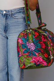 Colorful floral-patterned handbag held by a person wearing blue jeans.