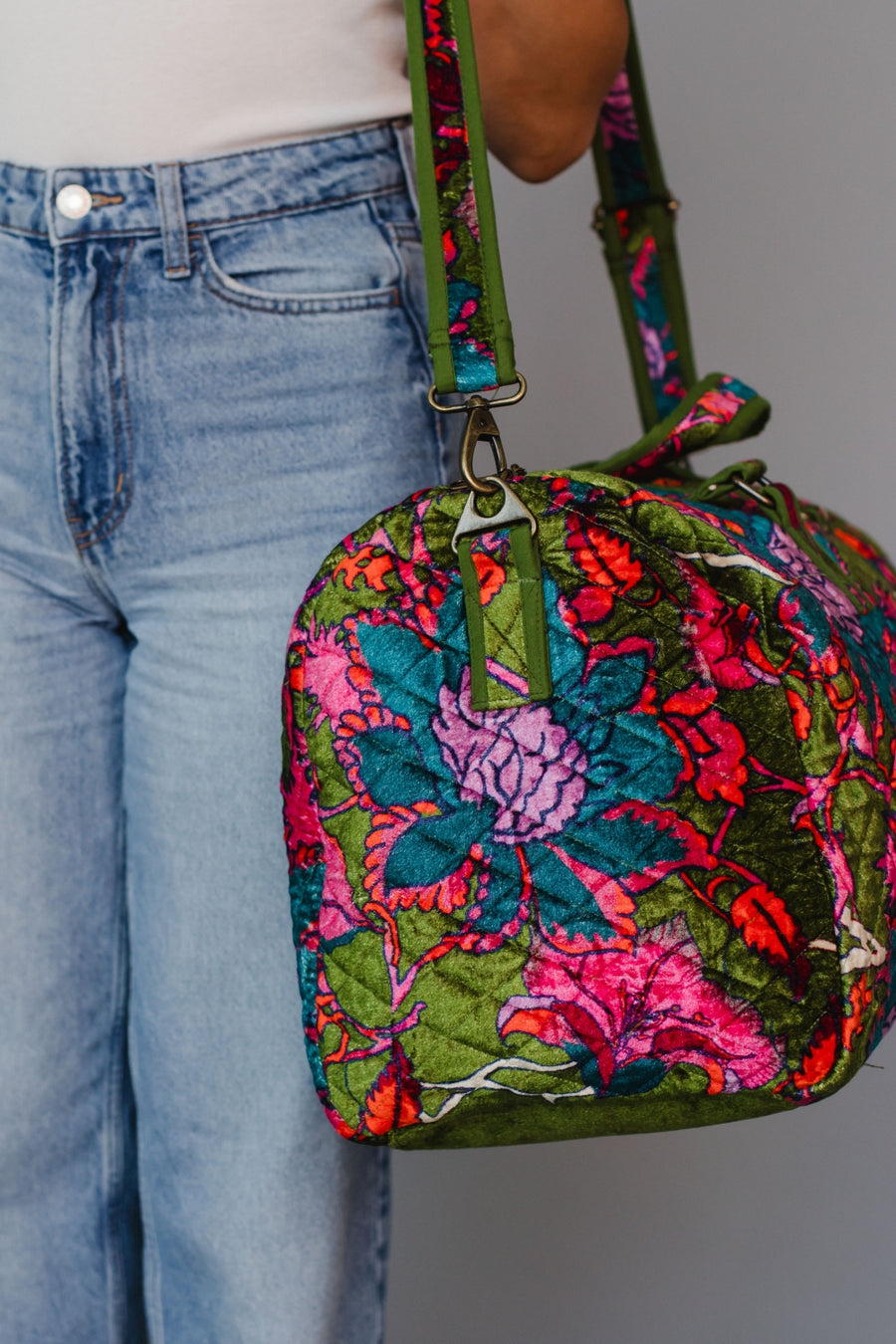 Colorful floral-patterned handbag held by a person wearing blue jeans.