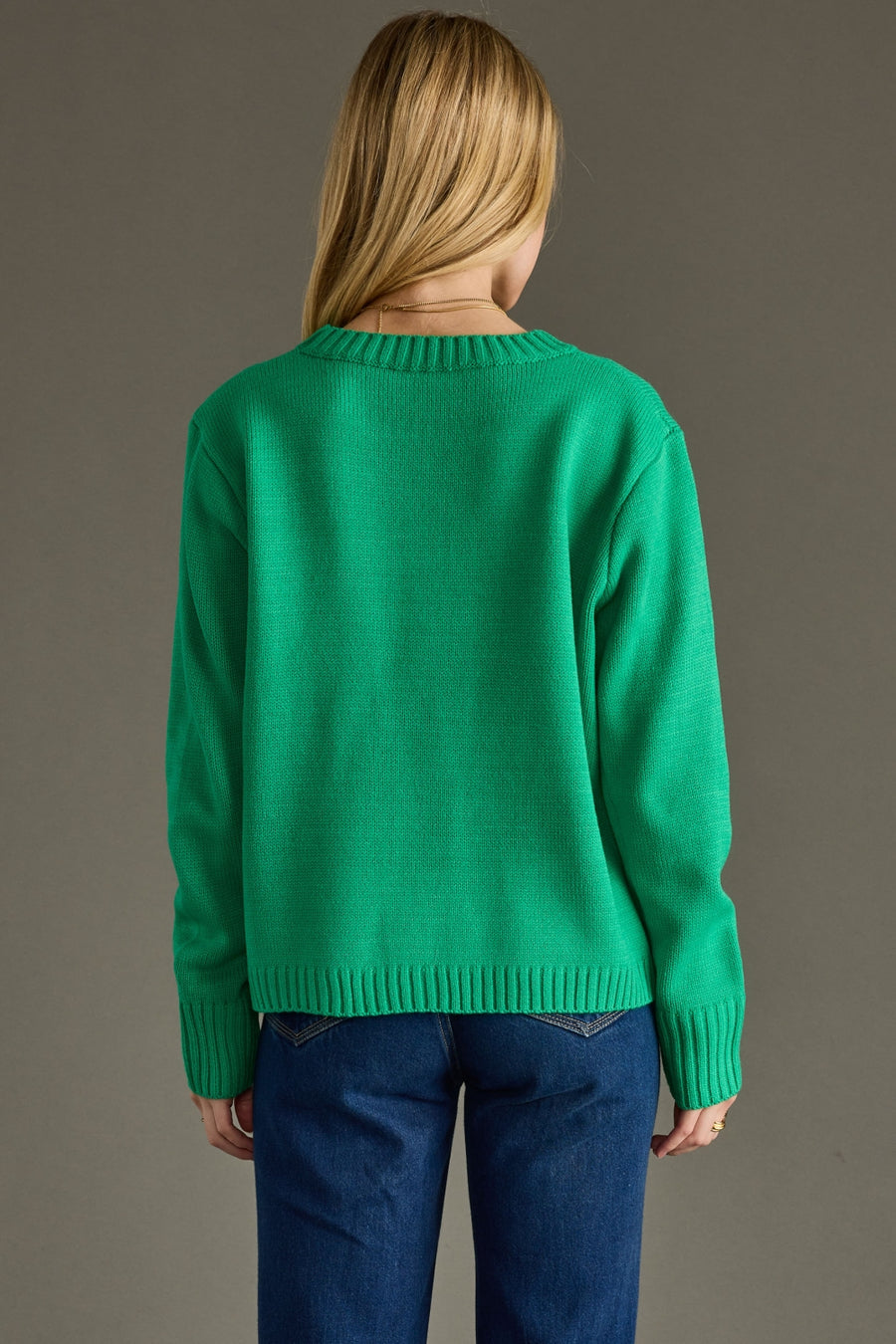 Person wearing a green sweater and blue pants on a gray background