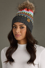 Woman wearing a colorful knit beanie with a pom-pom against a gray background