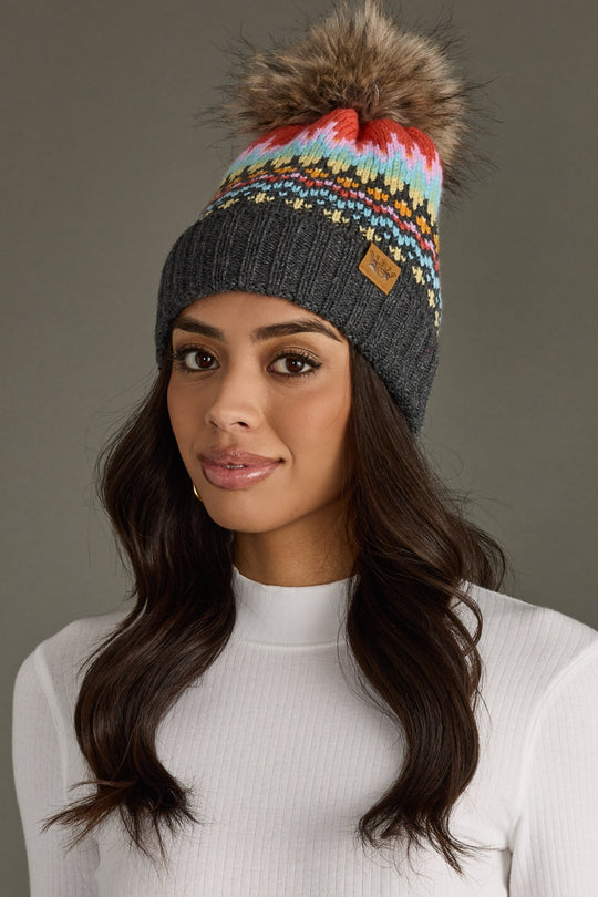 Woman wearing a colorful knit beanie with a pom-pom against a gray background