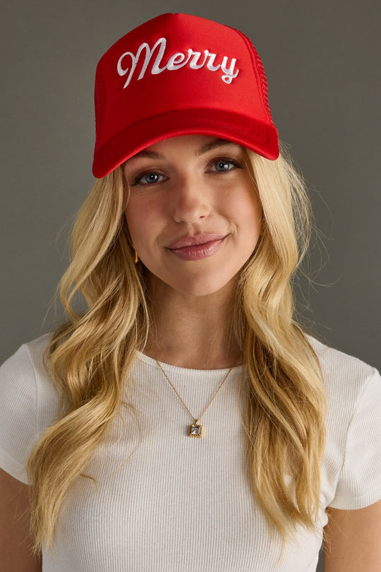 Woman wearing a red trucker hat with 'Merry' text on a gray background
