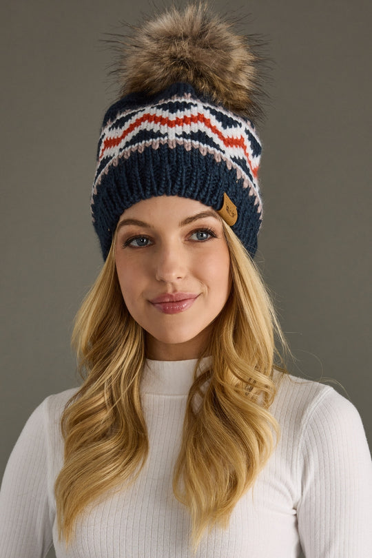 Woman wearing a knitted beanie with a fur pom-pom against a neutral background