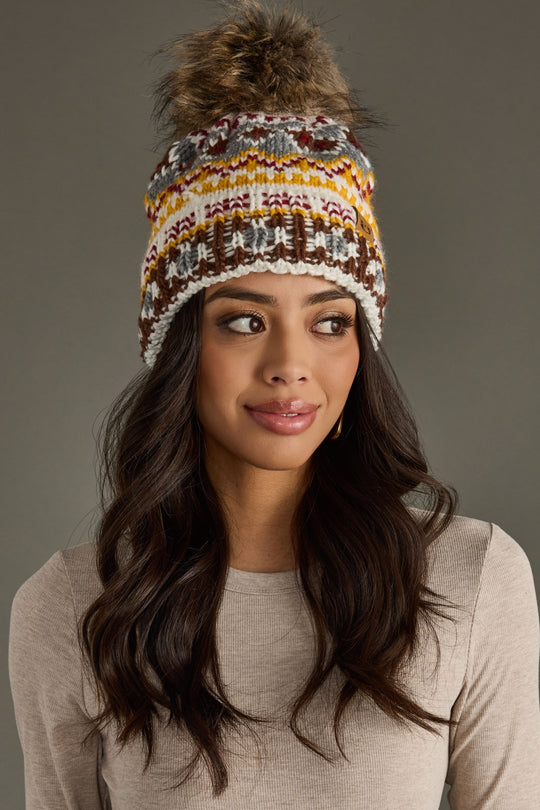 Woman wearing a patterned knit beanie with a fur pom-pom on a gray background