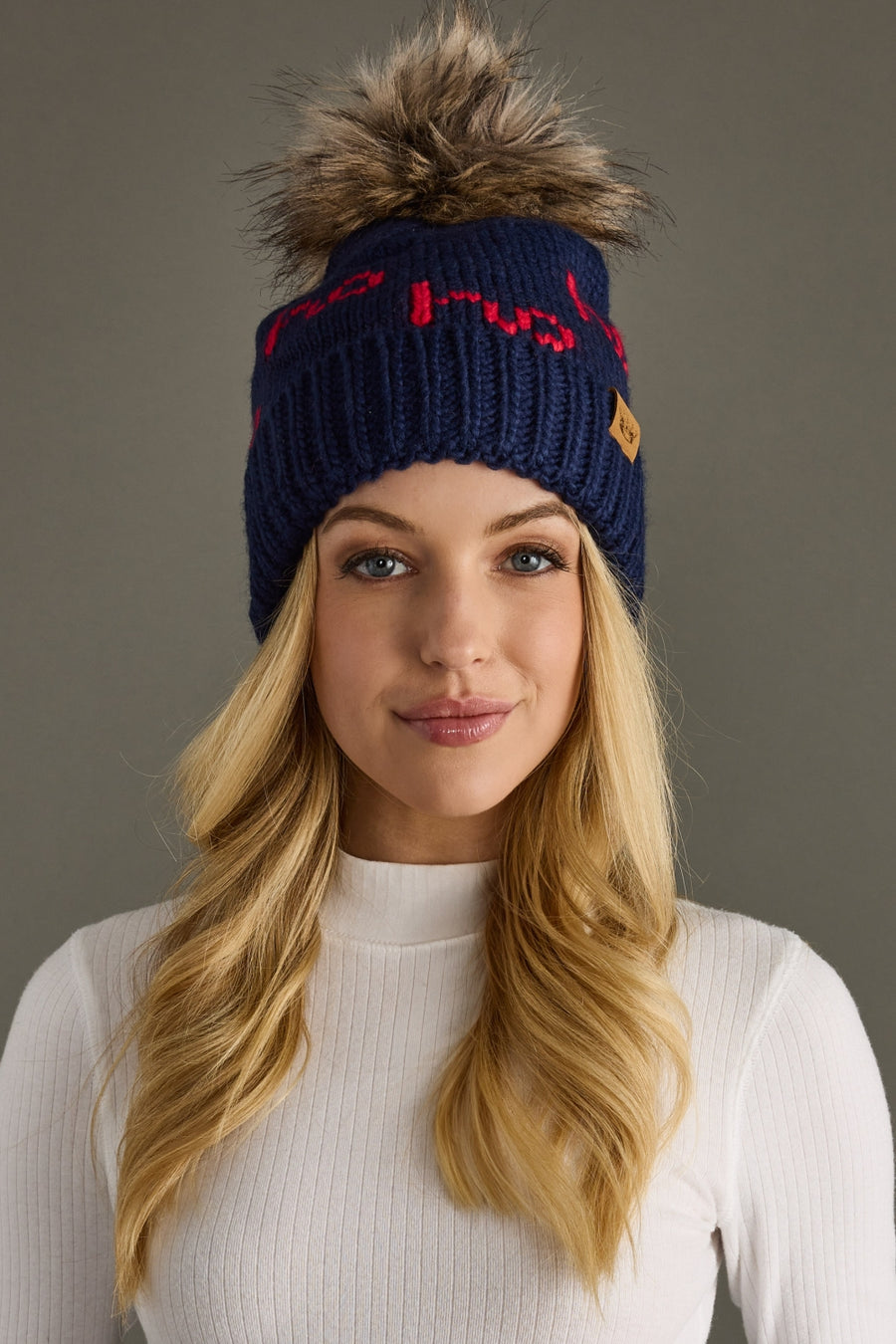 Woman wearing a navy blue beanie with a pom-pom on a gray background
