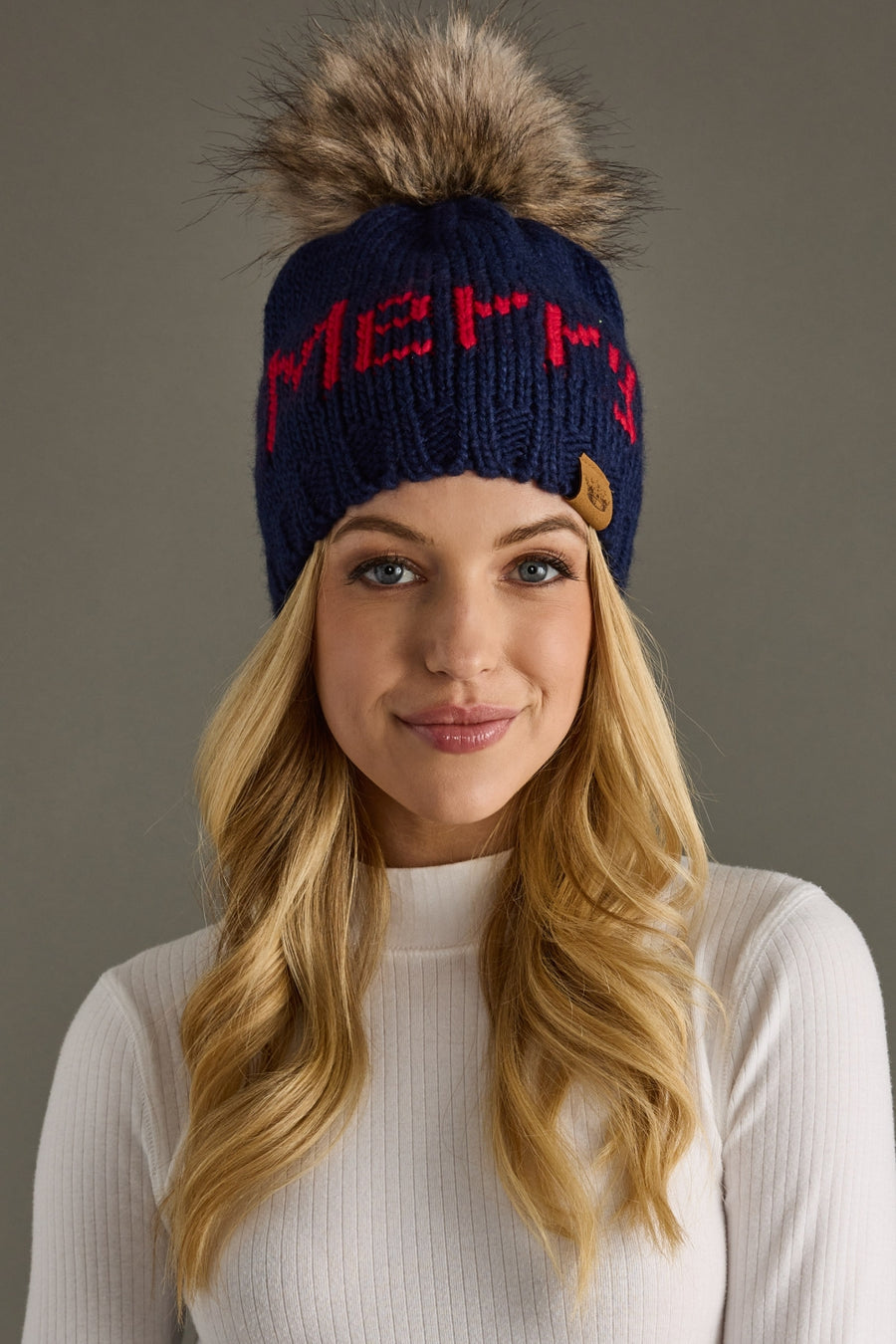Woman wearing a blue knit beanie with a fur pom-pom on a gray background
