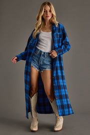 Woman wearing a blue plaid coat over a white top and denim shorts, standing against a gray background.