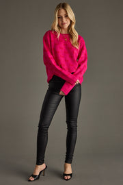 Woman wearing a bright pink sweater and black pants against a gray background
