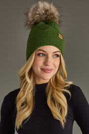 Woman wearing a green knit beanie with a fur pom-pom against a gray background