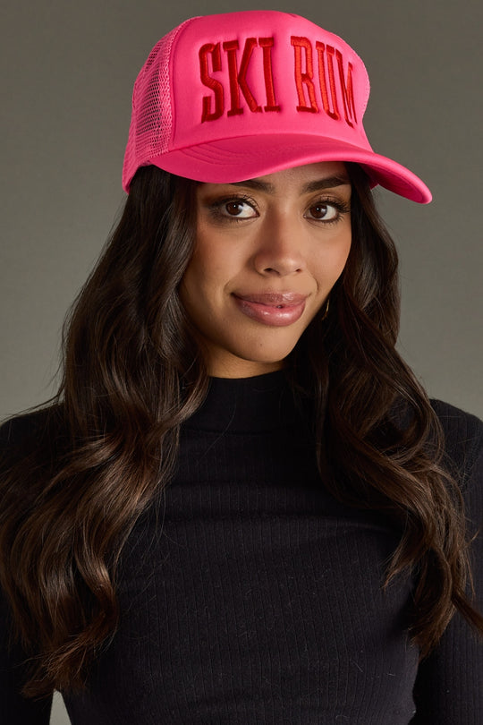 Woman wearing a pink cap with 'SKI BUM' text against a gray background