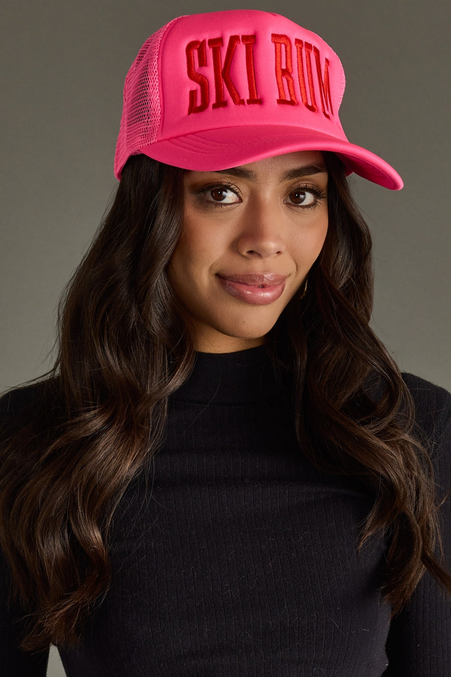 Woman wearing a pink cap with 'SKI BUM' text against a gray background