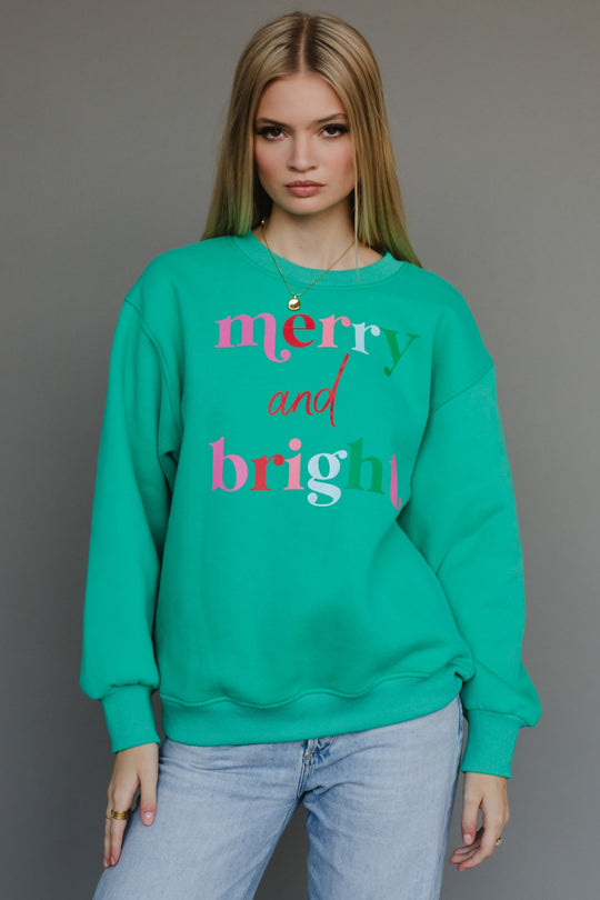 Person wearing a green sweatshirt with 'merry and bright' text on a gray background