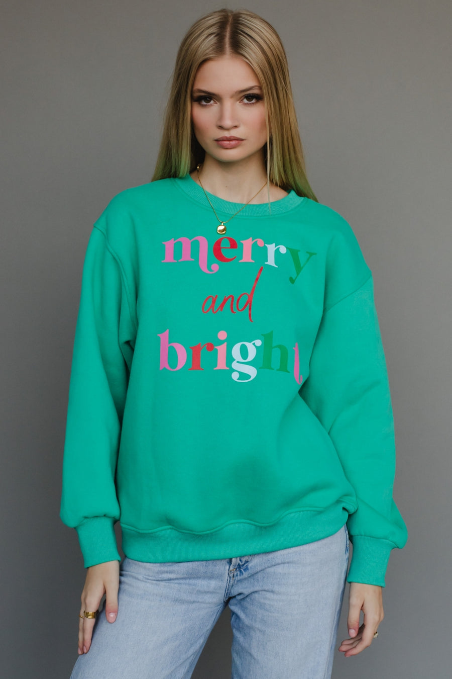 Person wearing a green sweatshirt with 'merry and bright' text on a gray background