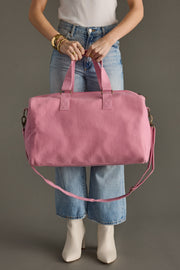 Person holding a pink duffel bag against a neutral background