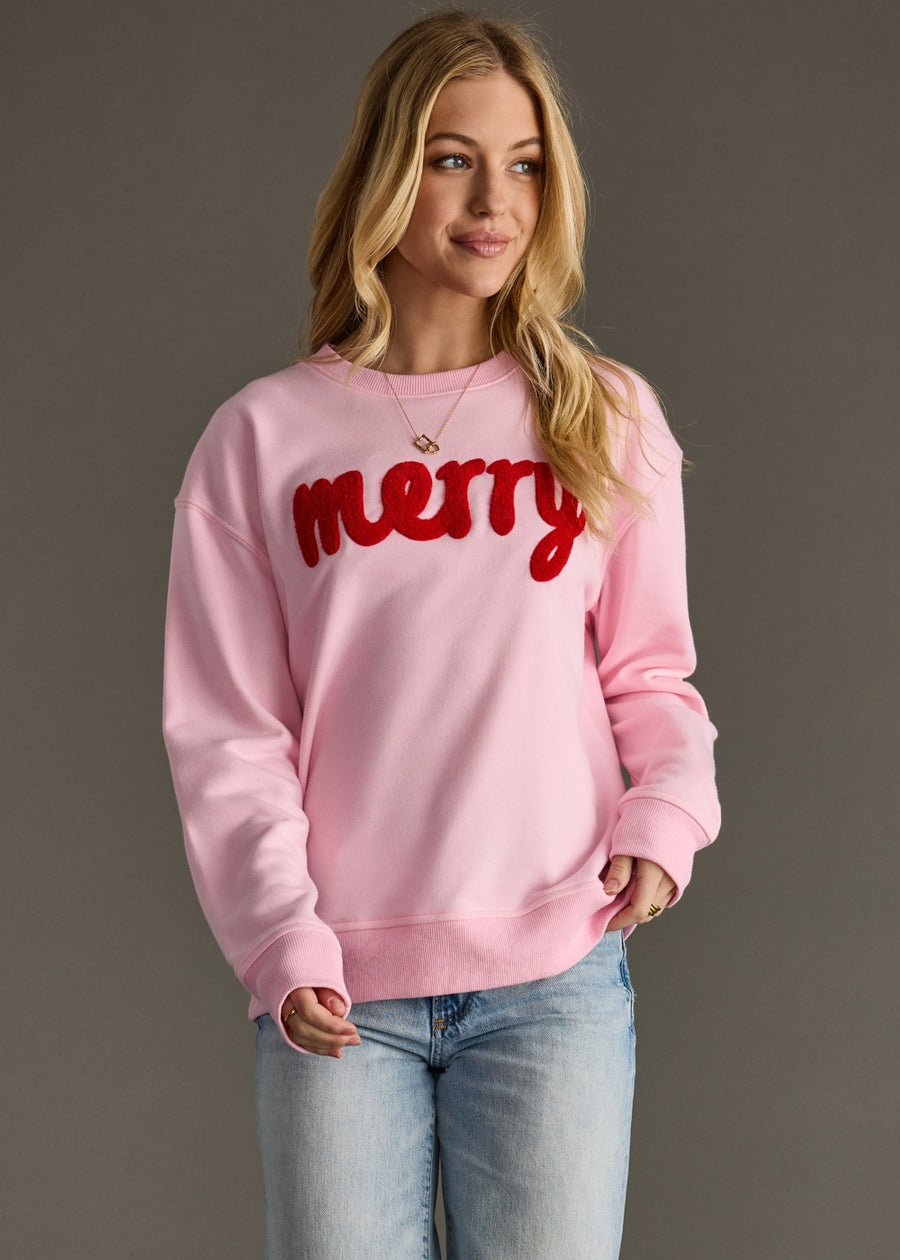 Woman wearing a pink sweatshirt with red 'merry' text against a gray background