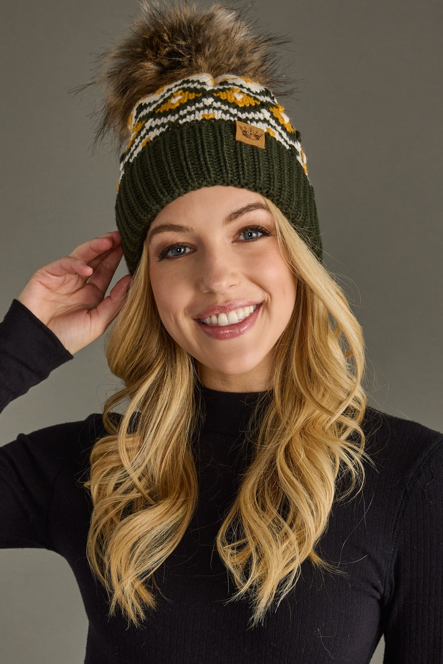 Woman wearing a green knit beanie with a fur pom-pom against a gray background