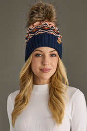 Woman wearing a navy blue beanie with a colorful pom-pom on a gray background