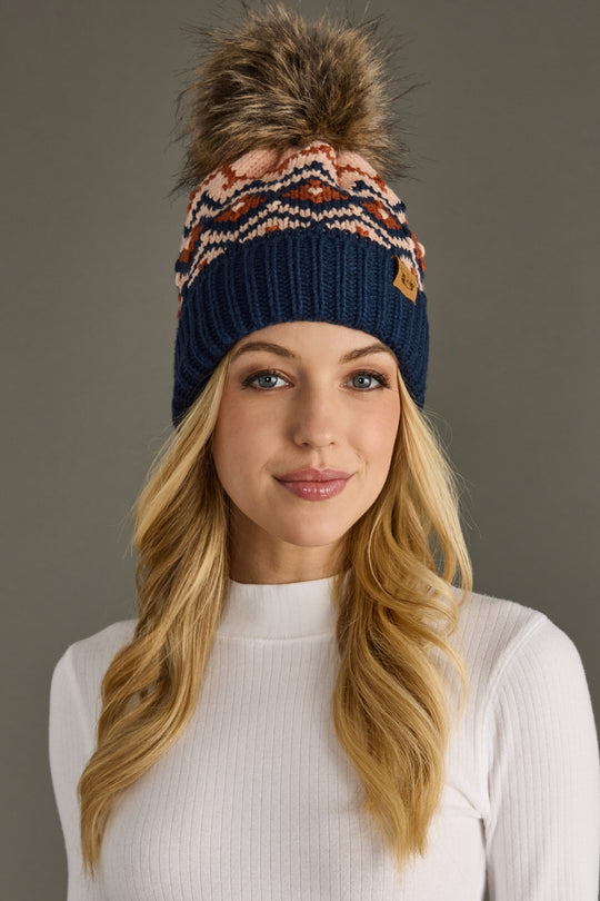Woman wearing a navy blue beanie with a colorful pom-pom on a gray background