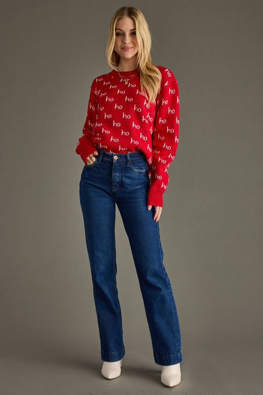 Woman wearing a red sweater with text and blue jeans on a gray background