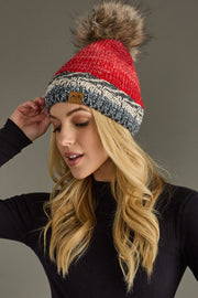 Woman wearing a red and gray knit beanie with a pom-pom on a gray background