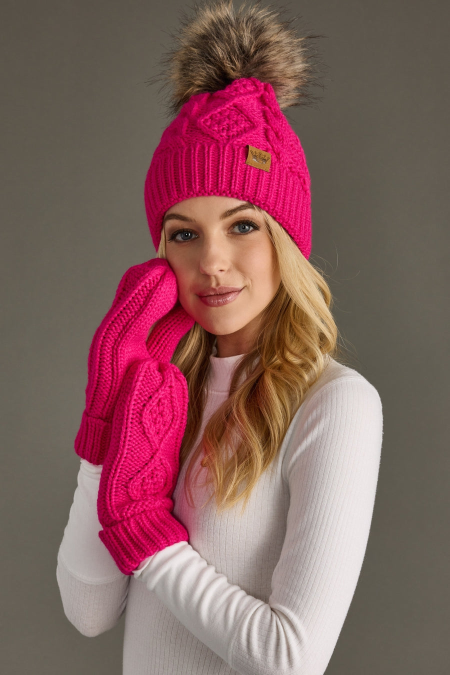 Woman wearing a pink knit hat and gloves against a gray background