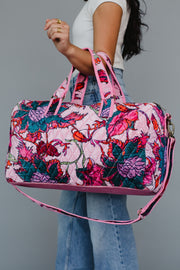 Floral patterned duffel bag held by a person against a gray background
