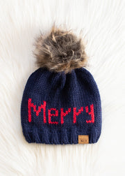 Navy blue knit beanie with red 'Merry' text and fur pom-pom on a white background