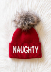 Red beanie with 'NAUGHTY' text and fur pom-pom on a white background