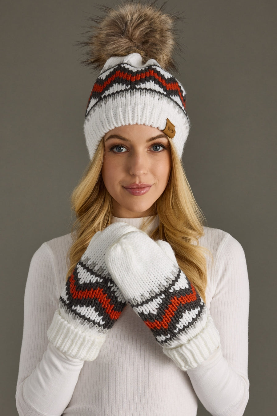 Woman wearing a white knit hat with a pom-pom and matching mittens on a gray background