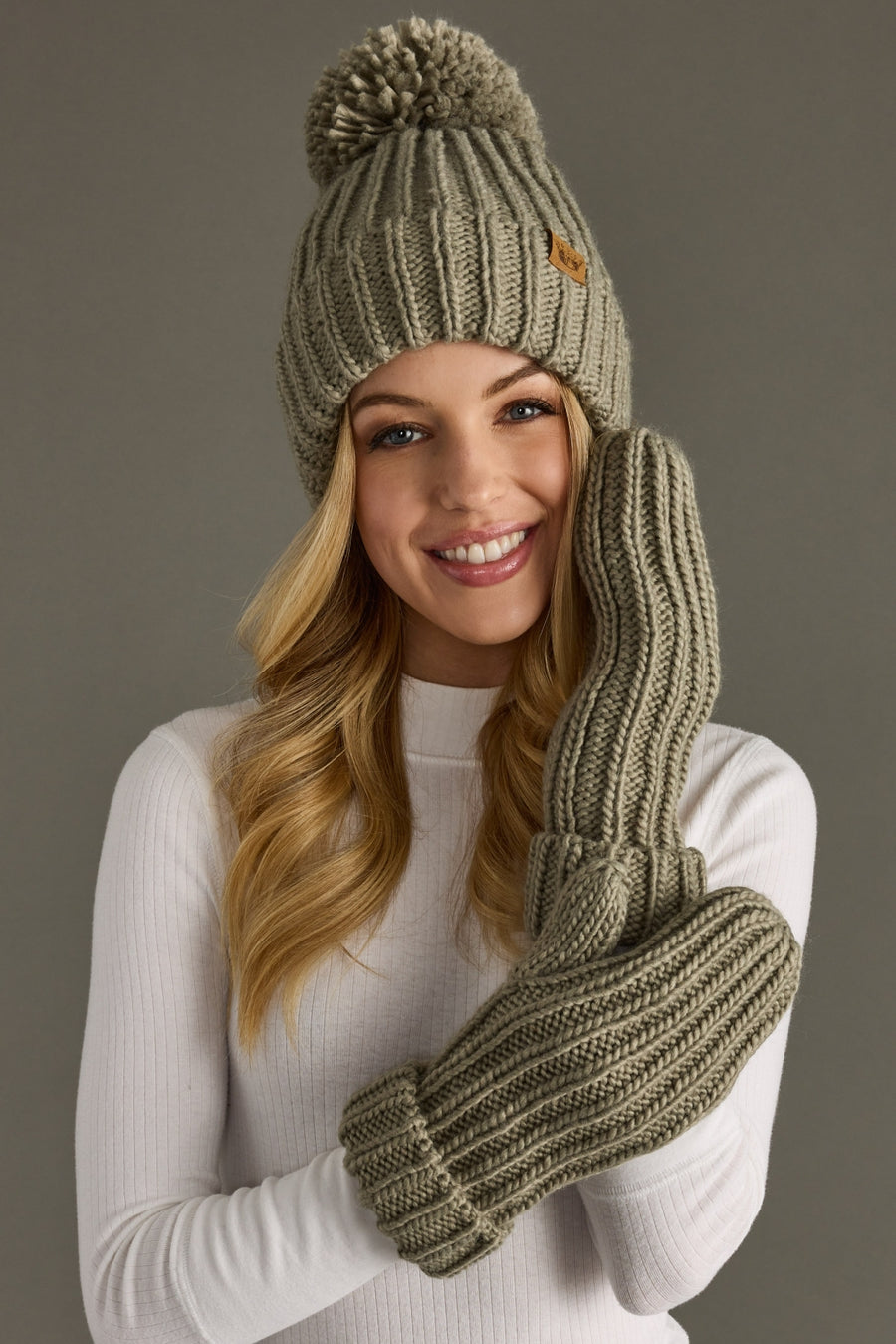 Woman wearing a matching knit beanie and gloves set against a neutral background