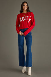 Woman wearing a red 'Merry' sweater and blue jeans on a gray background