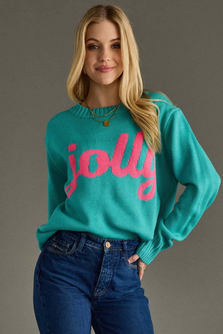 Woman wearing a teal sweater with pink text 'jolly' against a gray background