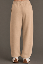 A person is shown from the back against a plain dark background, wearing Khaki Panache Sweatpants from the Panache Apparel Collection and white sneakers.