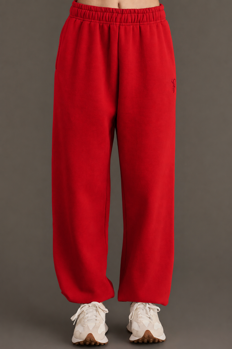 A person wearing Panache Apparel Collection’s Red Panache Sweatpants, featuring a relaxed fit and elastic waistband, paired with white sneakers, stands against a plain gray background.