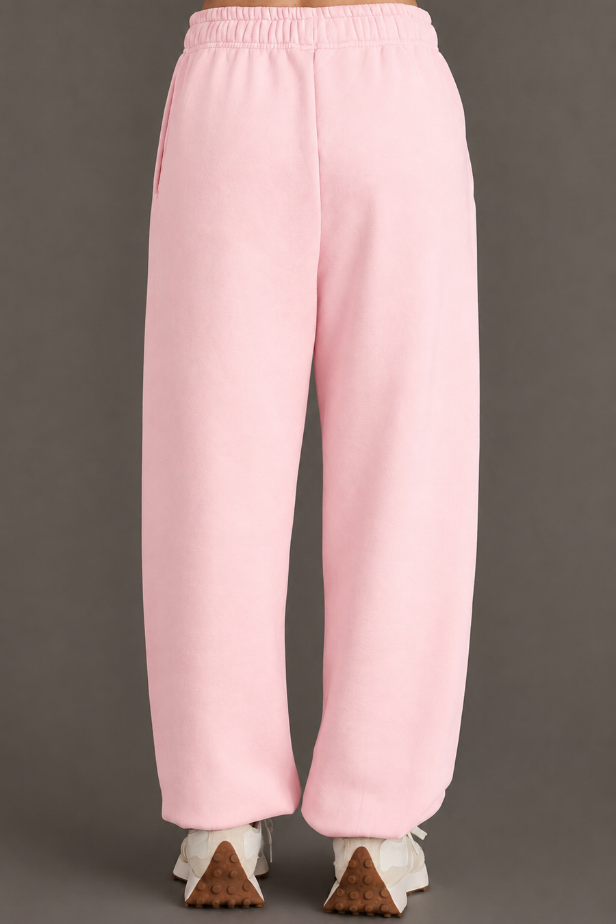 A person wearing Panache Apparel Collection’s Light Pink Panache Sweatpants and white sneakers is shown from the back, standing against a plain gray background.