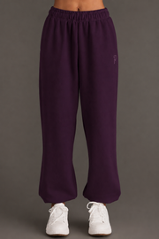 A model showcases the Panache Apparel Collection Plum Panache Sweatpants, featuring a relaxed fit and elastic waistband, paired with white sneakers. The photo displays only the lower torso and legs against a simple, neutral background.