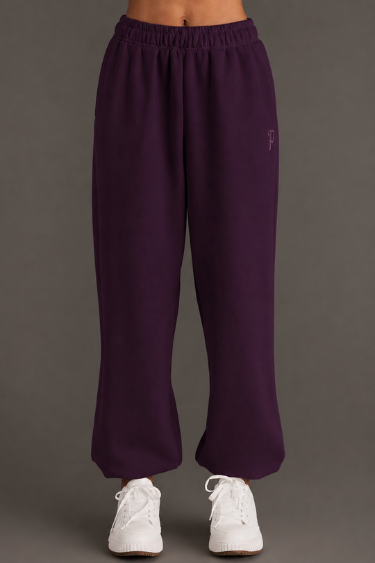 A model showcases the Panache Apparel Collection Plum Panache Sweatpants, featuring a relaxed fit and elastic waistband, paired with white sneakers. The photo displays only the lower torso and legs against a simple, neutral background.