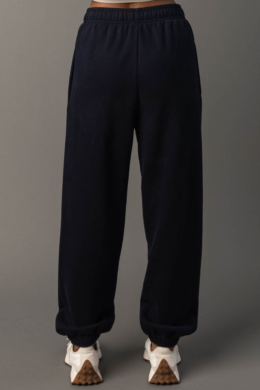 A person wearing Dark Navy Panache Sweatpants from Panache Apparel Collection and white sneakers stands against a plain gray background. The image is taken from behind, showcasing the back view of the sweatpants and shoes.