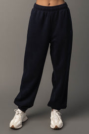 A person is seen wearing loose-fitting Dark Navy Panache Sweatpants from the Panache Apparel Collection and white sneakers, standing against a plain gray background. Their upper body is not visible.