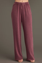 A person wearing the Panache Apparel Collection Merlot Washed Soft Sweatpants, which are high-waisted, loose-fitting, and feature pockets in a mauve hue, stands against a plain background with only their lower torso and legs visible.