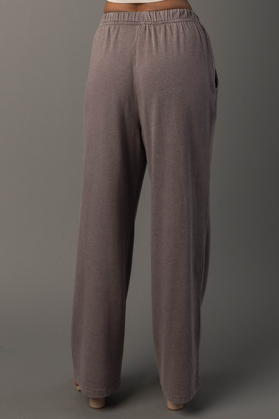 A person wearing Panache Apparel Collection’s Gray Washed Soft Sweatpants. Featuring a loose fit, high waist, wide legs, and an elastic waistband, and stands against a plain gray background.
