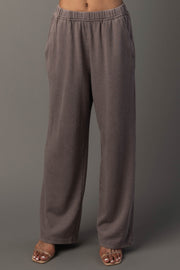A person wearing the Panache Apparel Collection’s Gray Washed Soft Sweatpants, which are loose and high-waisted with pockets, along with open-toed sandals, stands against a plain gray background. Their upper body is not visible.