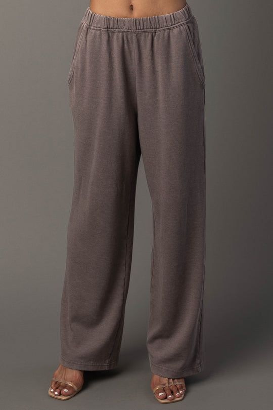 A person wearing the Panache Apparel Collection’s Gray Washed Soft Sweatpants, which are loose and high-waisted with pockets, along with open-toed sandals, stands against a plain gray background. Their upper body is not visible.
