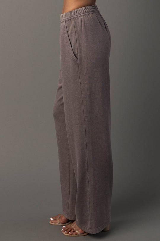 A person wearing Panache Apparel Collection’s Gray Washed Soft Sweatpants and clear sandals stands sideways against a plain gray background.