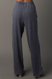 A person is shown from the back against a plain gray background, modeling Panache Apparel Collection’s Slate Blue Washed Soft Sweatpants. Only the lower torso and legs are visible, highlighting the loose fit, high waist, and elastic waistband of the pants.