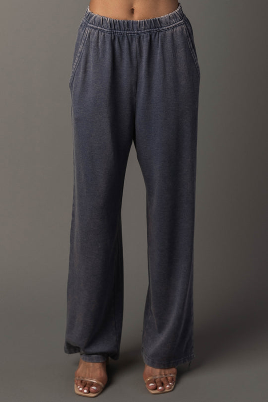 A person wearing loose-fitting, slate blue washed soft sweatpants with pockets from Panache Apparel Collection and clear high-heeled sandals, standing against a neutral background.