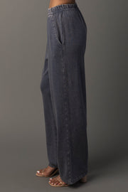 A person wearing loose-fitting, Slate Blue Washed Soft Sweatpants with pockets from Panache Apparel Collection and tan heeled sandals, standing against a plain gray background.
