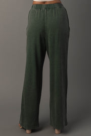 A person is wearing the Pine Green Washed Soft Sweatpants by Panache Apparel Collection, featuring a loose, relaxed fit and a high-rise elastic waistband, while standing against a plain gray background. These sweatpants offer comfortable style ideal for casual wear.