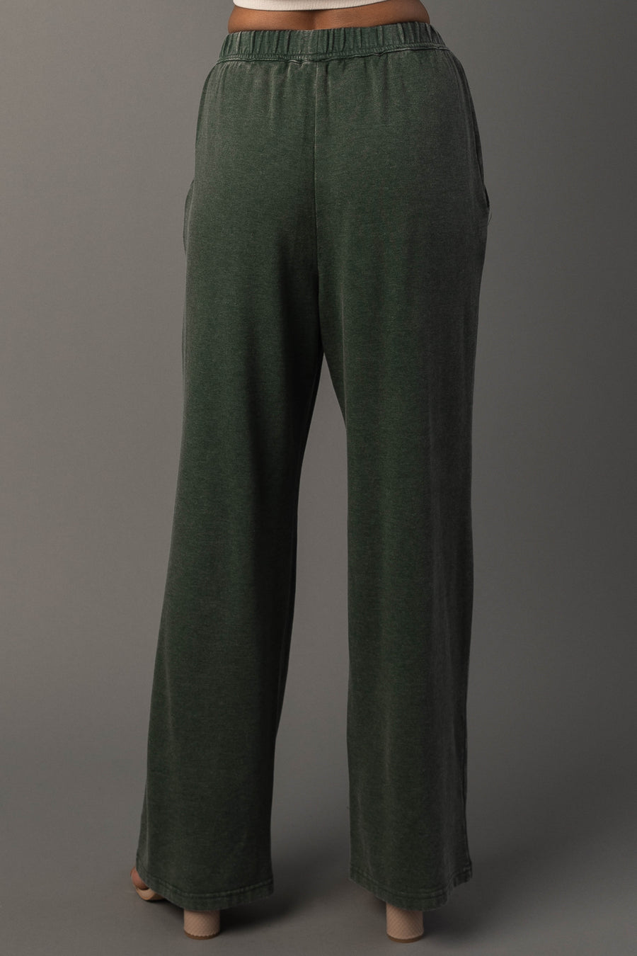 A person is wearing the Pine Green Washed Soft Sweatpants by Panache Apparel Collection, featuring a loose, relaxed fit and a high-rise elastic waistband, while standing against a plain gray background. These sweatpants offer comfortable style ideal for casual wear.