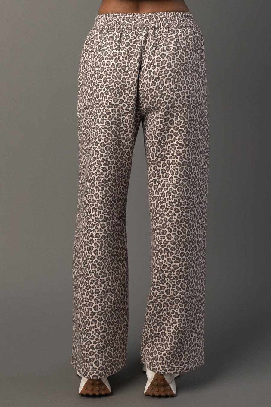A person is shown from the waist down wearing Panache Apparel Collection’s Cream & Brown Leopard Sweatpants, standing against a plain gray background.